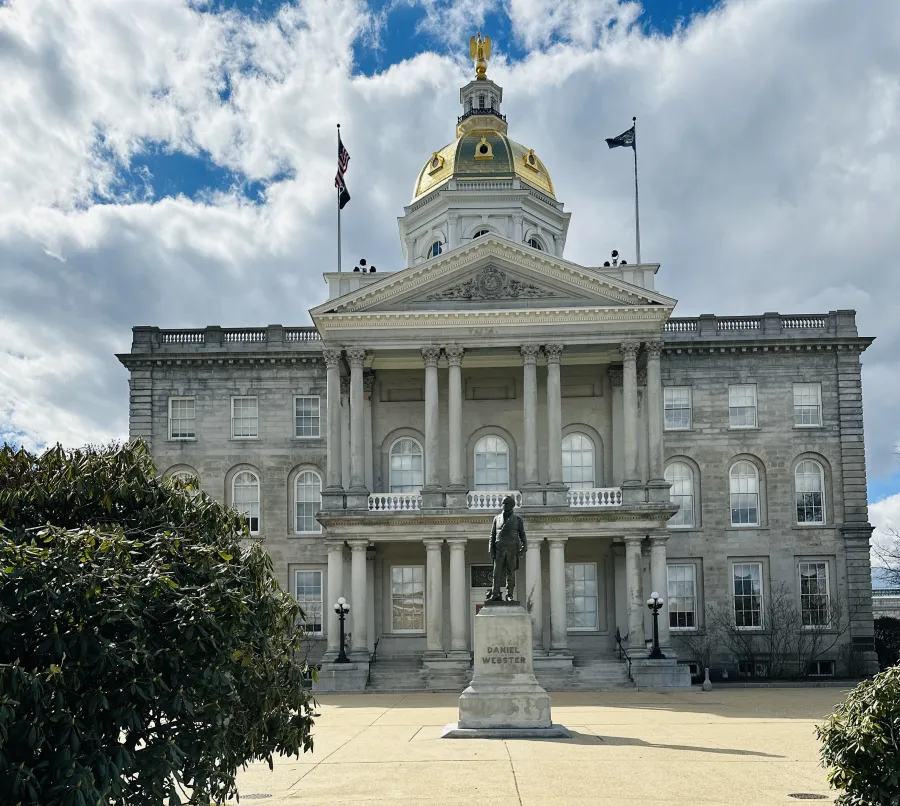 a large white building with a statue in front of it with New Hampshire State House in the background
