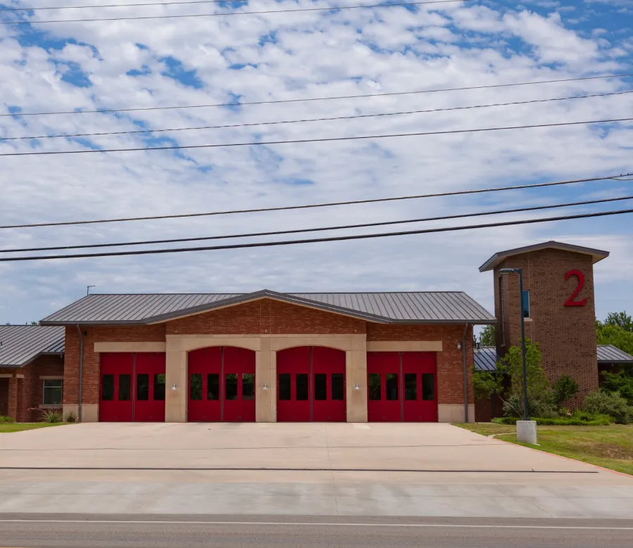 Modern fire station with red garage doors and a large number 2 on the tower under a partly cloudy sky