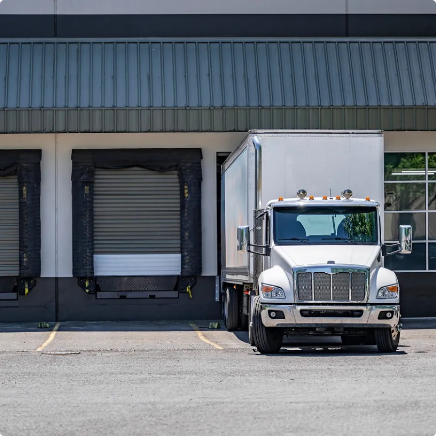 White delivery truck parked at loading dock of industrial warehouse building on sunny day