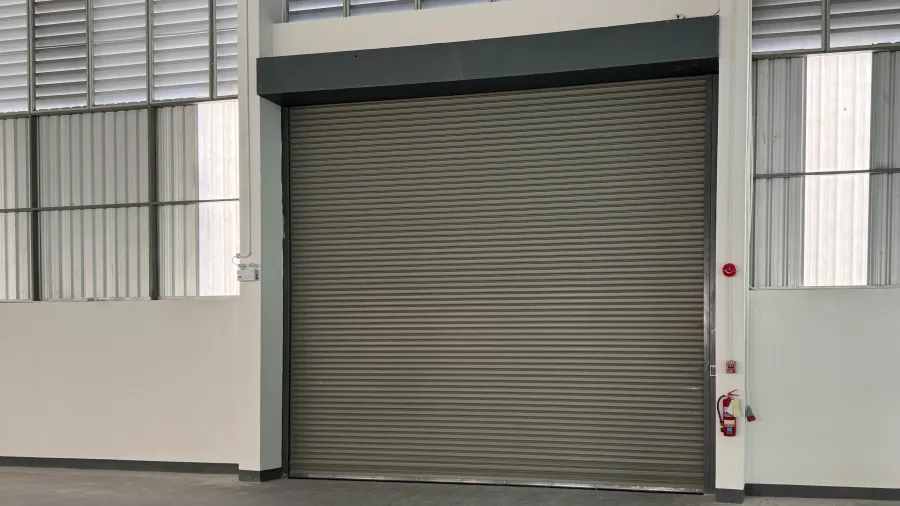Closed gray industrial metal roll-up door inside a spacious warehouse with concrete floor and white walls.