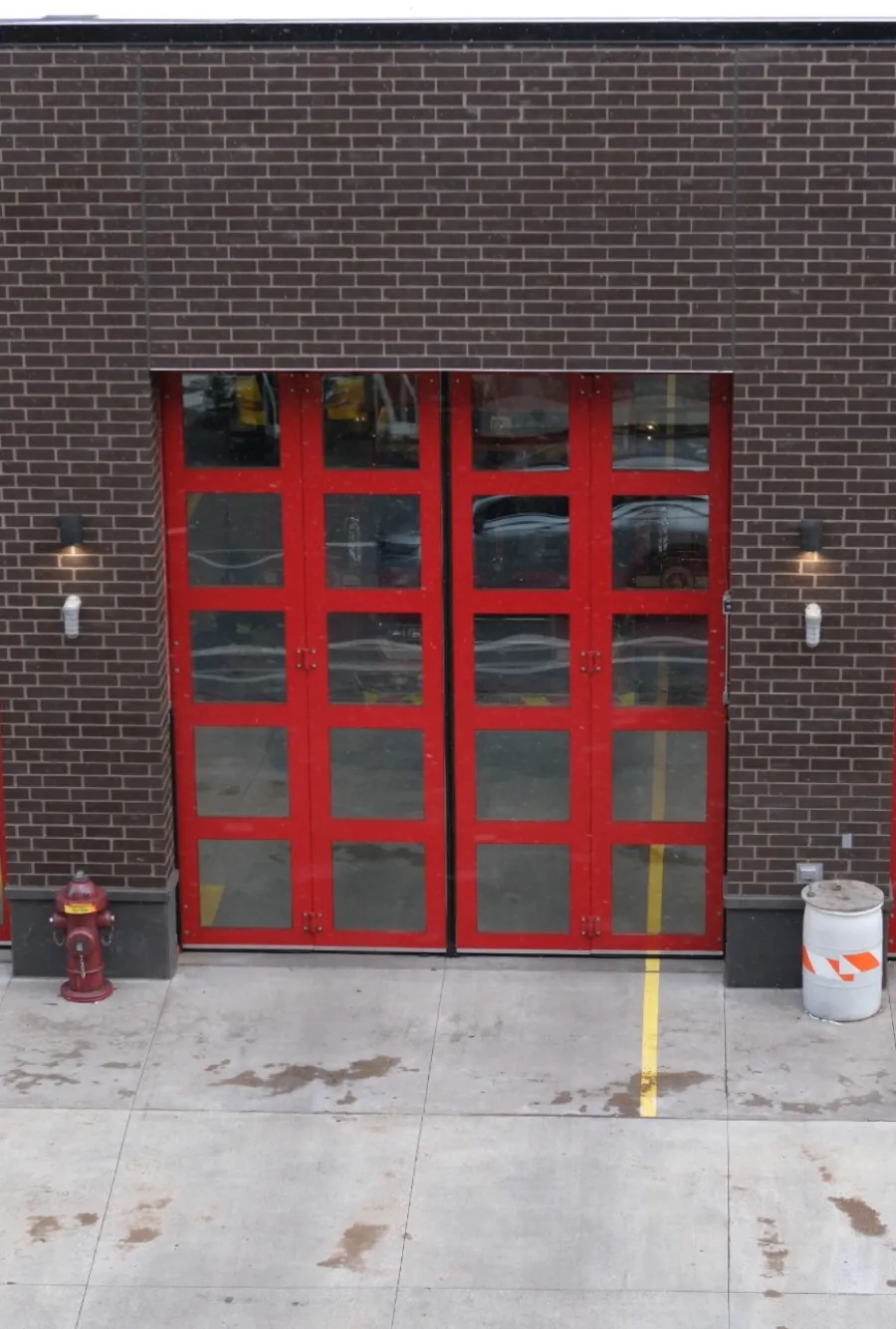 Three red paneled garage doors on a brown brick building with concrete pavement and a fire hydrant outside.