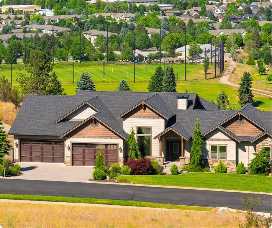 Modern suburban house with large garage, landscaped front yard, and green golf course in the background.