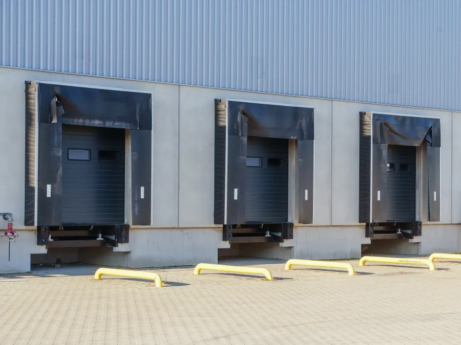 Three industrial loading dock doors with black seals at a warehouse exterior under bright daylight.