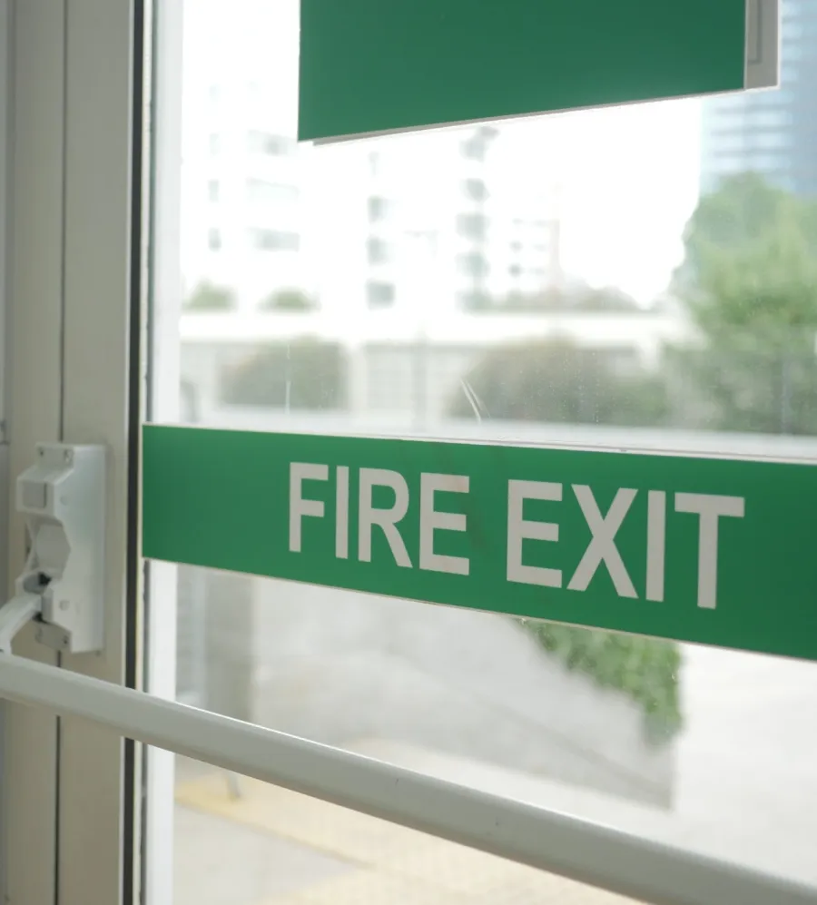 Close-up of glass fire exit doors with green signage in a modern building showing emergency exit path.