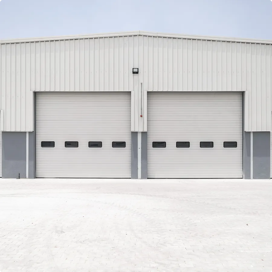 Two closed white industrial garage doors on a modern warehouse building with paved ground in front.