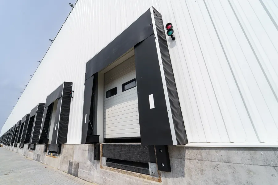 Empty industrial loading dock bays with closed white overhead doors and black seals on a warehouse building.