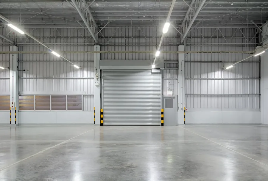 Spacious empty industrial warehouse with concrete floor and closed metal roller door under bright ceiling lights