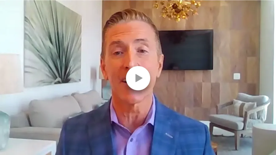 Man in blue blazer speaking in a modern living room with neutral tones and decorative artwork.