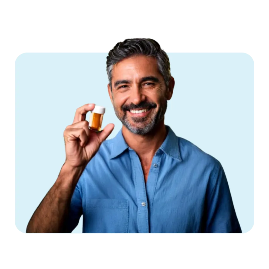 Smiling man in blue shirt holding a small amber medicine bottle with white cap against light blue background