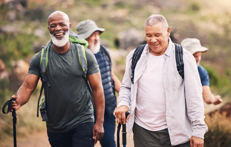 Group of happy middle-aged men hiking outdoors with backpacks and walking sticks on a trail.