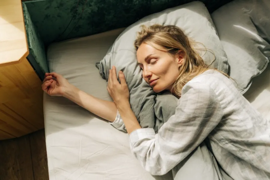 Woman sleeping peacefully on a bed hugging a pillow with natural sunlight streaming in