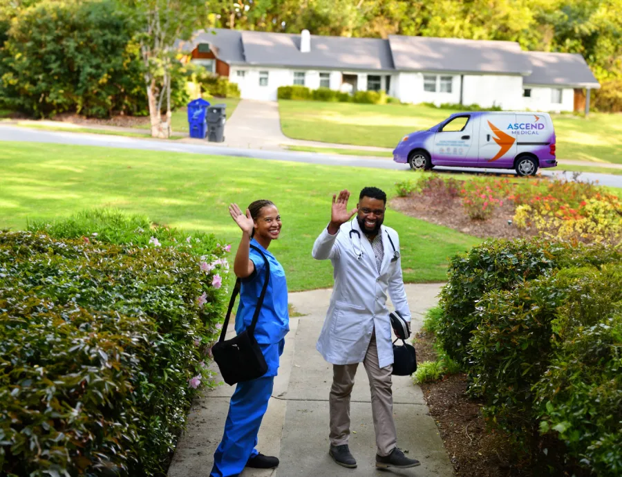 Healthcare team waving from a home entrance, with a service van in the background.