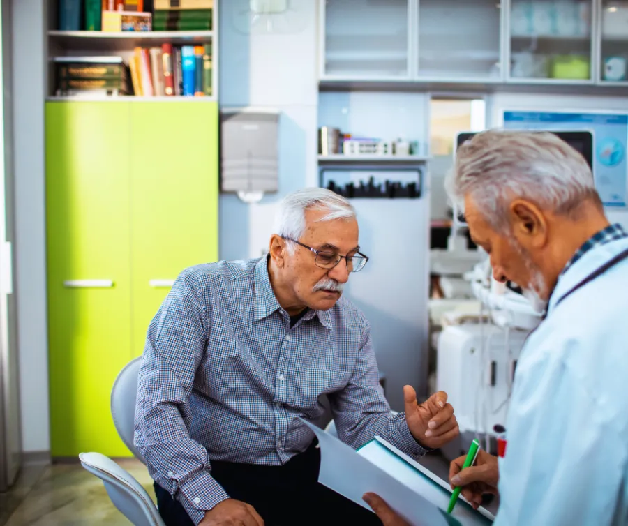 Senior man consulting with doctor in medical office discussing health documents together.
