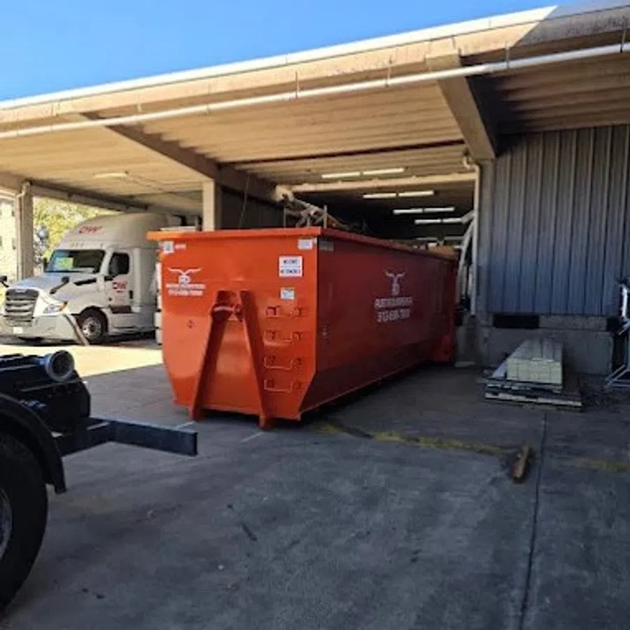Large orange dumpster container parked in an industrial loading dock area on a sunny day.
