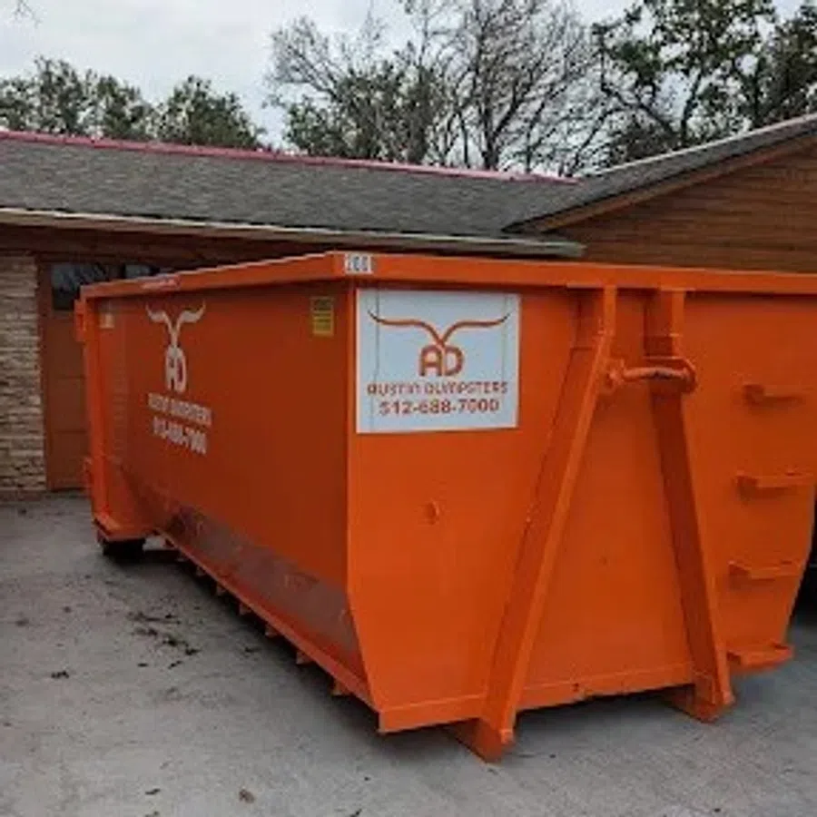 Large orange Austin Dumpsters container placed on a concrete driveway near a house with trees in the background.