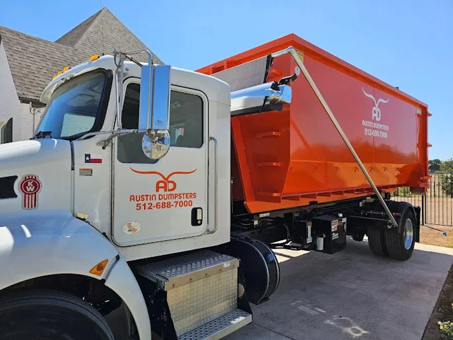 White and orange Austin Dumpsters truck parked outdoors under clear blue sky near a residential area.