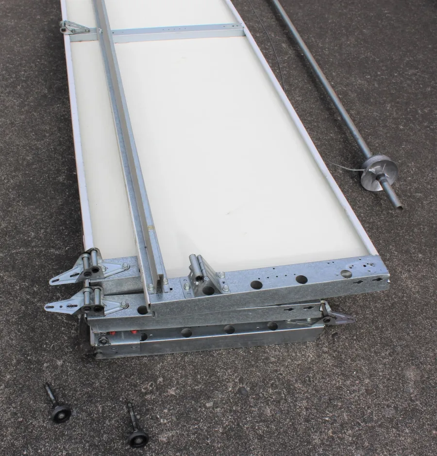 Metal framing and white panel parts with screws and a metal rod on concrete surface for assembly.