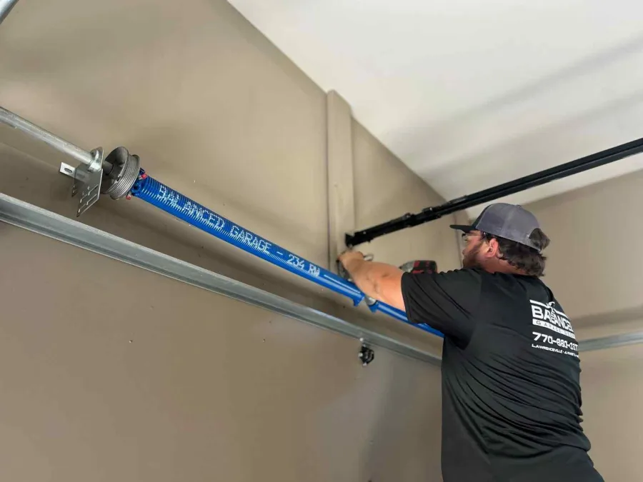 Technician installing or repairing a blue garage door torsion spring inside a residential garage.