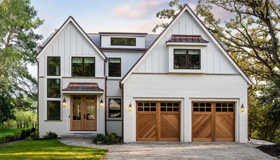 Modern white brick house with wooden garage doors and entryway set in a lush green yard at sunset.