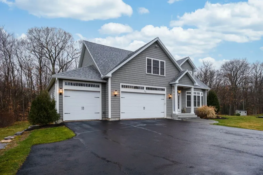 Modern gray house with double garage, surrounded by trees and a clear blue sky.