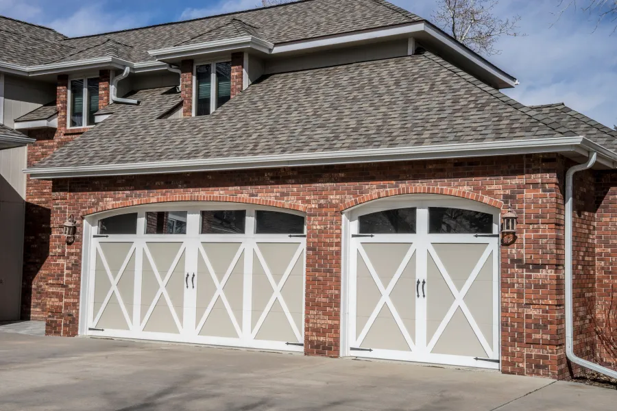 Elegant brick garage with white doors and arched windows, framed by a clear blue sky.