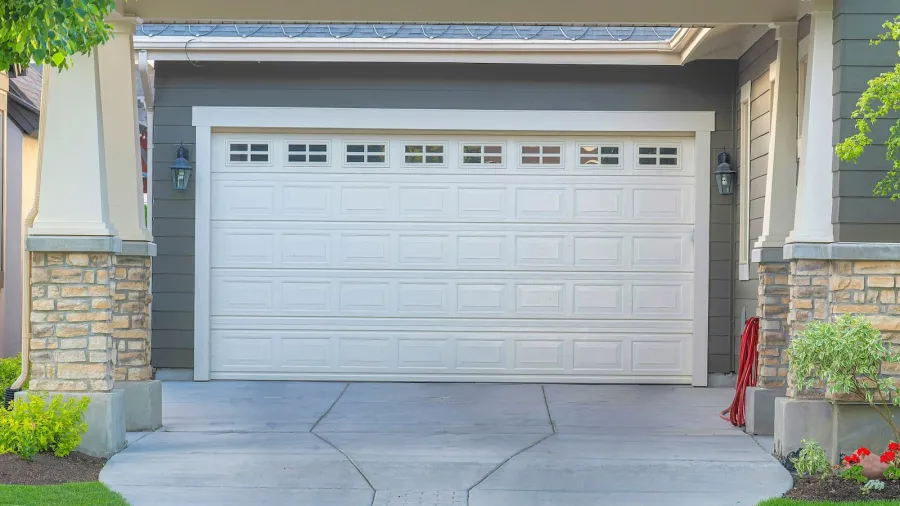 Front view of a modern white garage door with windows, stone pillars, and a concrete driveway.
