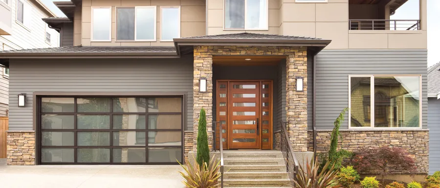 Modern home exterior featuring wooden door, stone accents, and large windows with a landscaped entrance.