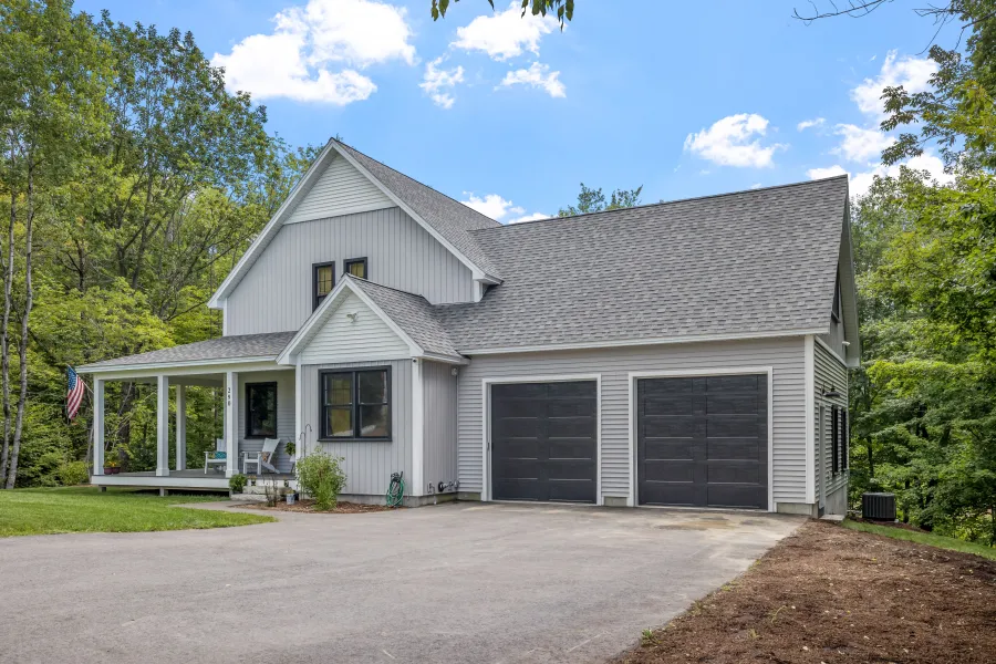 Charming modern home with a spacious driveway, lush greenery, and a welcoming porch under a clear blue sky.