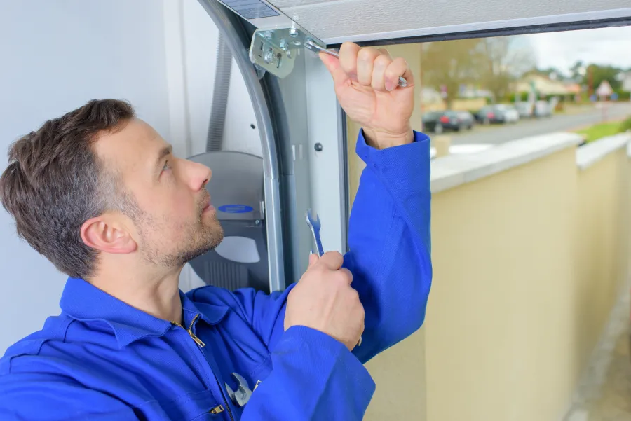 Technician in blue coveralls repairing garage door with wrench during daytime installation work