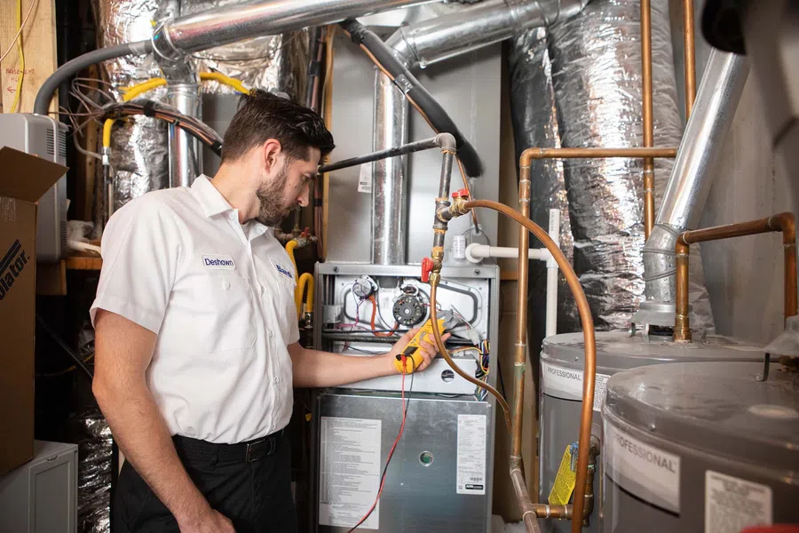 Technician checking a furnace in a residential basement with tools and equipment.