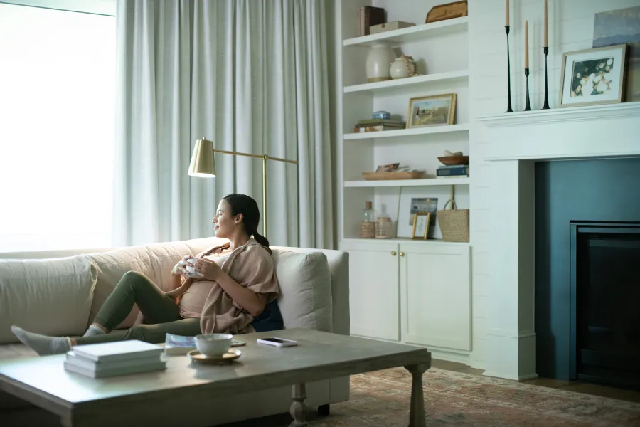 A woman relaxes on a sofa, enjoying a cozy moment with a snack in a bright, modern living room.