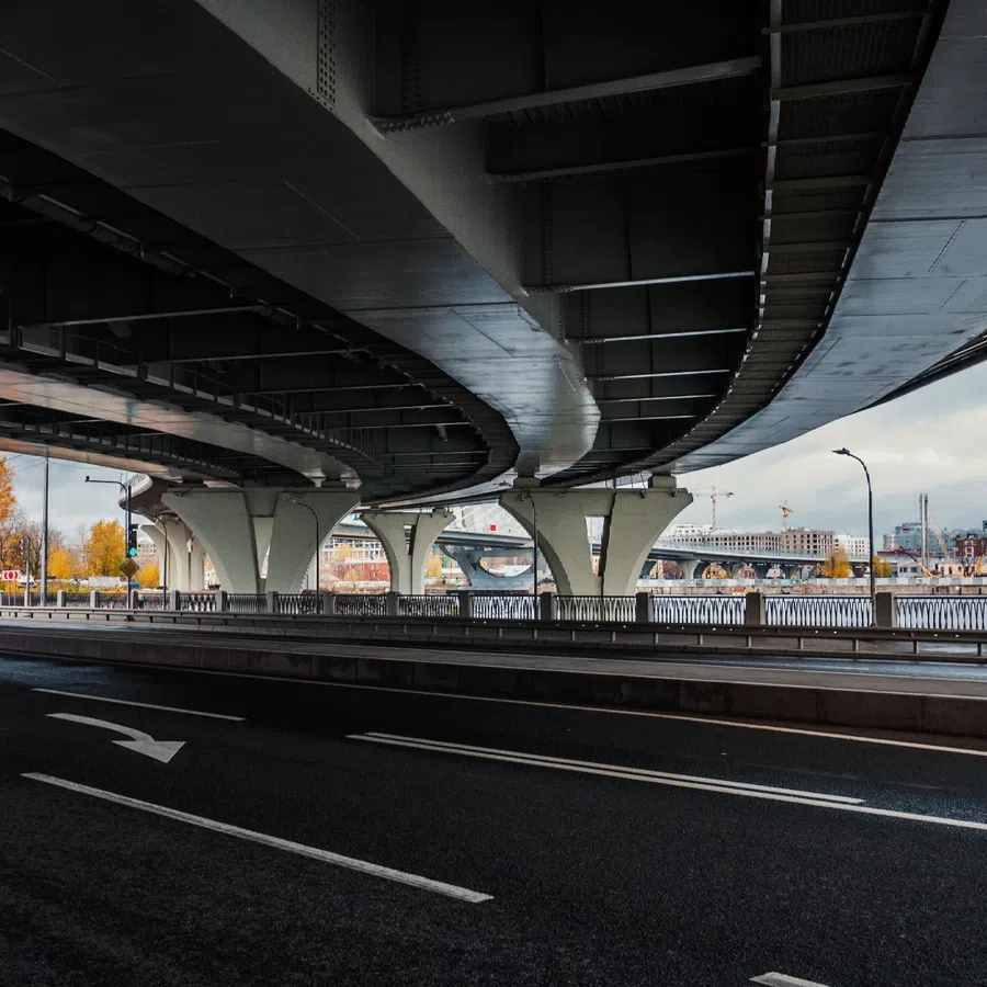 Empty road beneath a curved modern overpass with cityscape and river in the background on a cloudy day