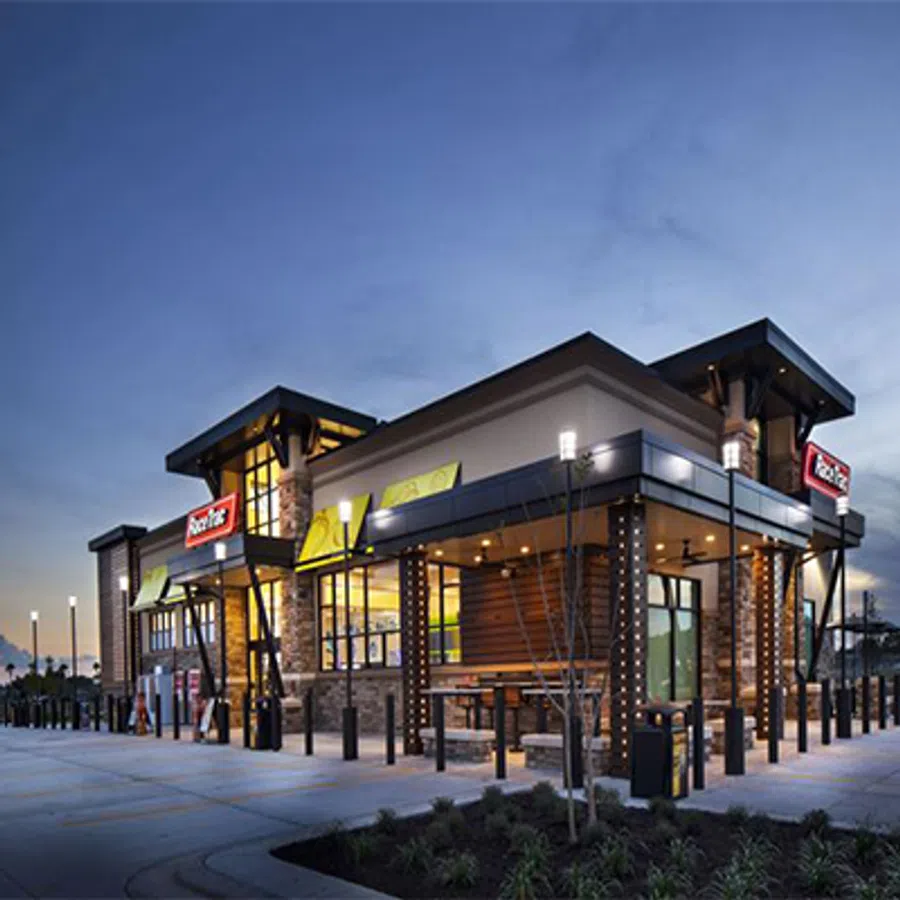 Modern fast-food restaurant building at dusk with illuminated signage and outdoor seating area.