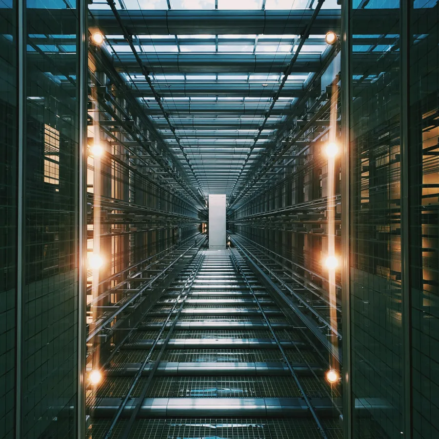 Looking up inside a modern glass elevator shaft with lights and metal framework in urban building.