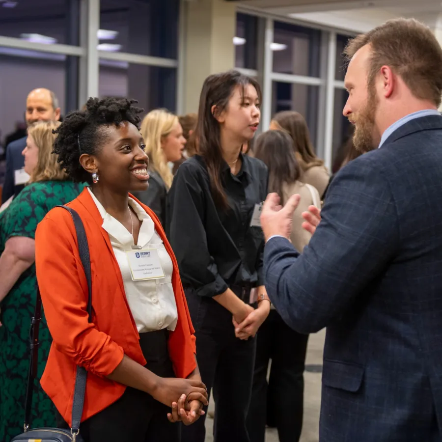 Diverse professionals networking and conversing in a modern office event with bright lighting and large windows.