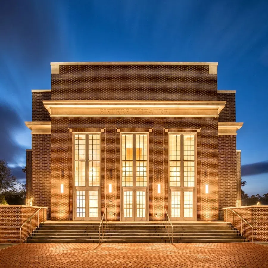 Illuminated brick building with large windows and stairs under deep blue evening sky.