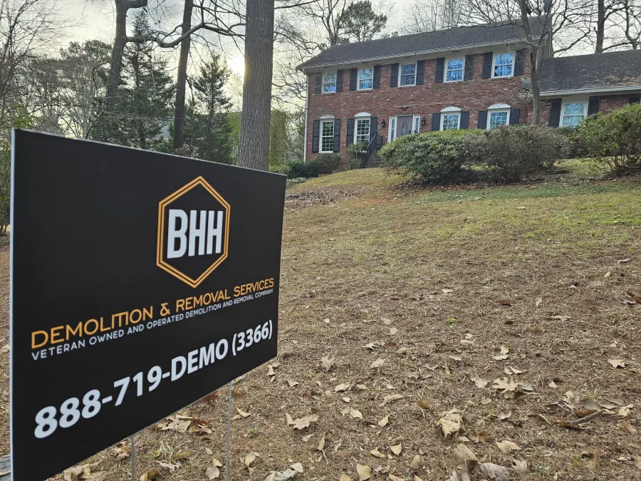 BHH Demolition & Removal Services sign on yard with brick colonial house in background during daytime.