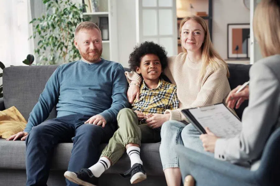 Smiling family with a child sitting on a couch during a counseling session with a professional.