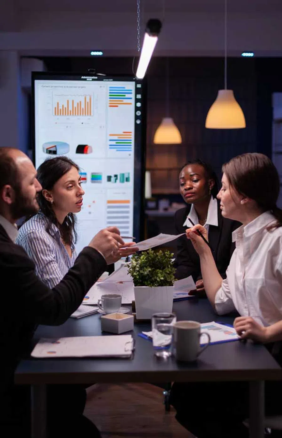 Team of business professionals discussing data charts during a meeting in a modern office at night.