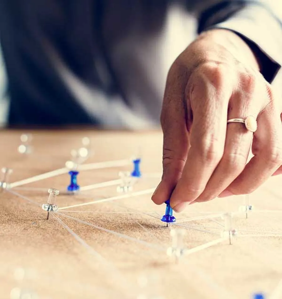 Hand placing a blue pushpin on a corkboard connected by white strings forming a network pattern.