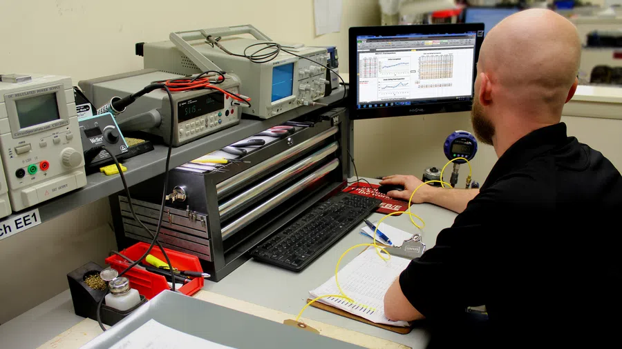 Technician analyzing data on computer screen with electronic testing equipment in laboratory workspace