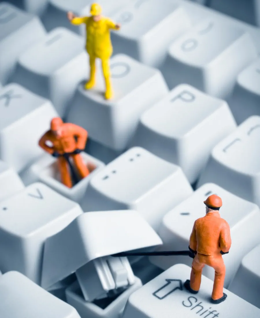Miniature construction workers repairing or removing a key on a white computer keyboard close-up.
