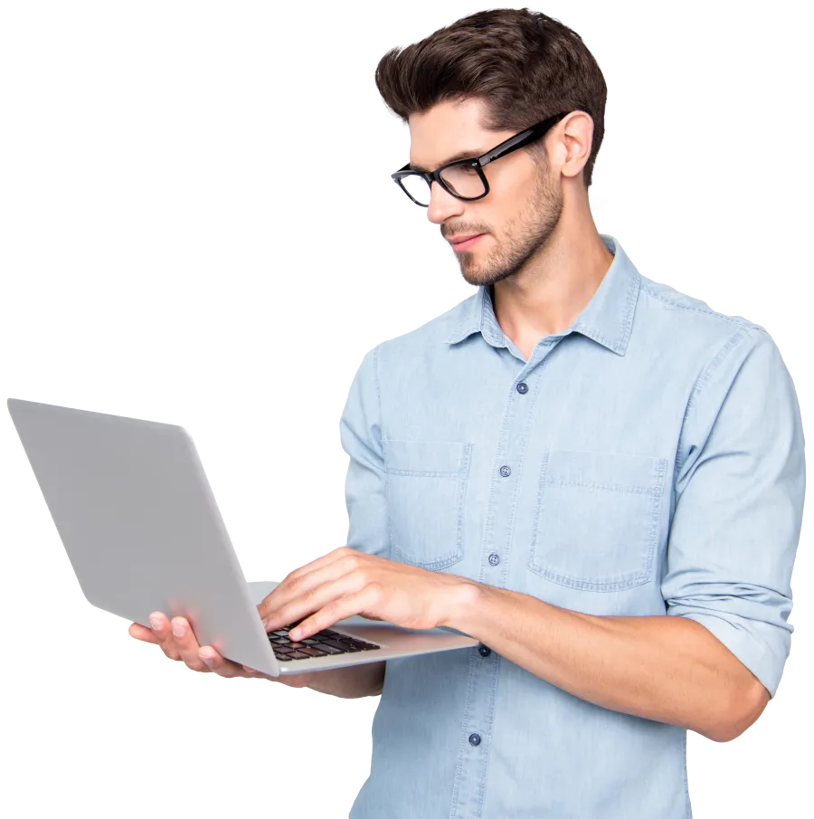 Young man in glasses and light blue shirt working on a laptop with focused expression