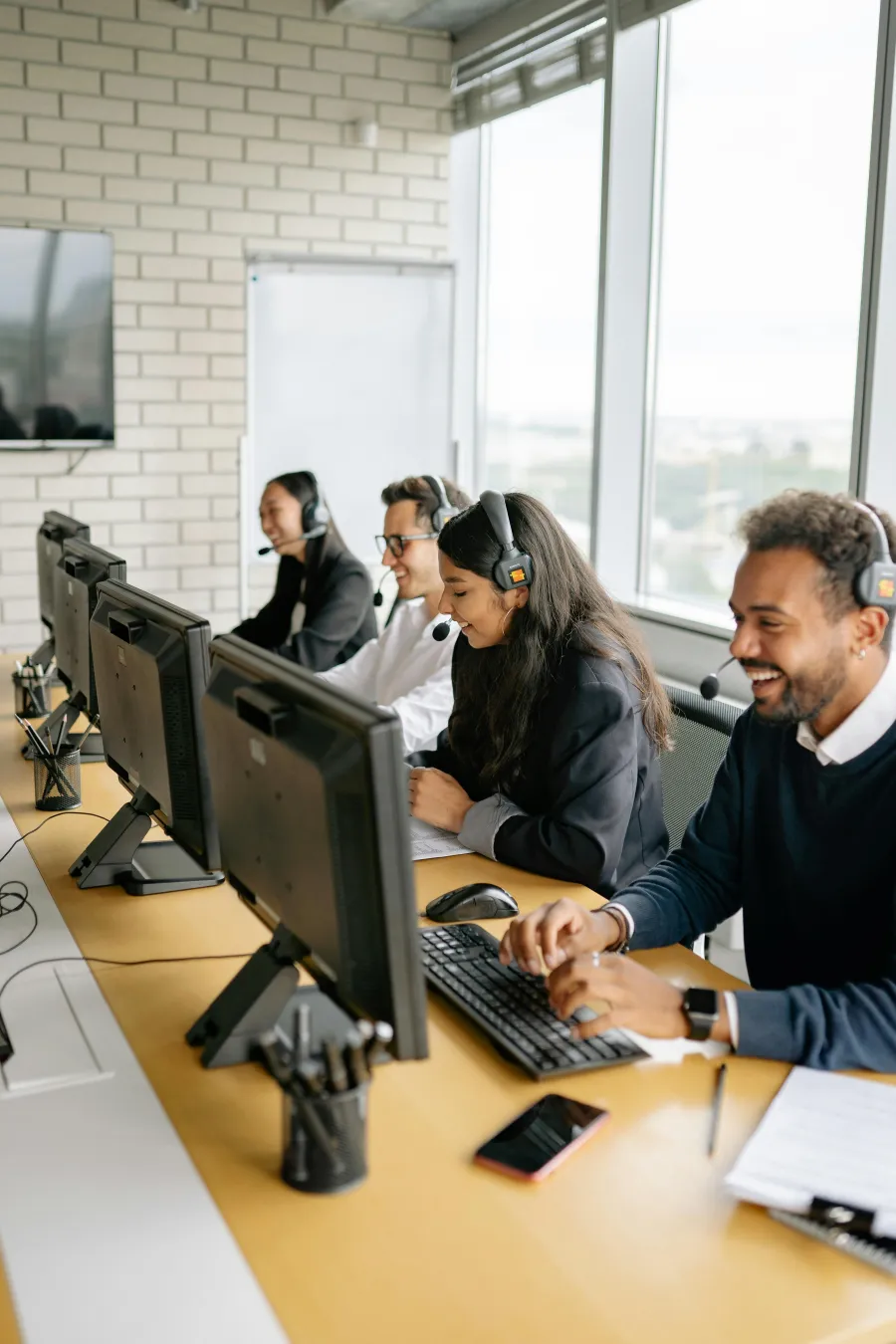 Call center team wearing headsets working on computers and assisting customers in a modern office environment.