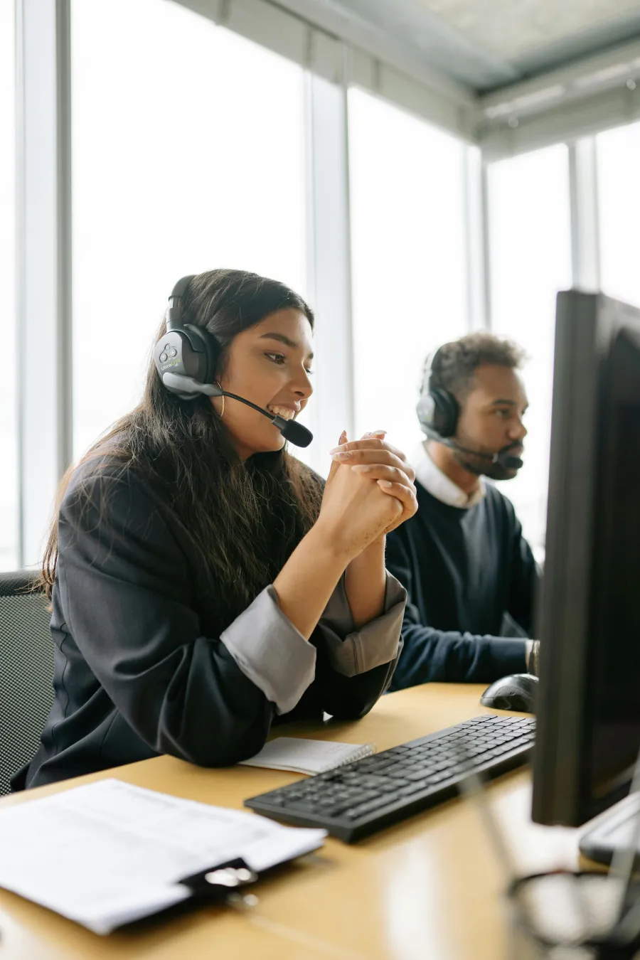 Two customer service representatives wearing headsets working at computers in a modern bright office.