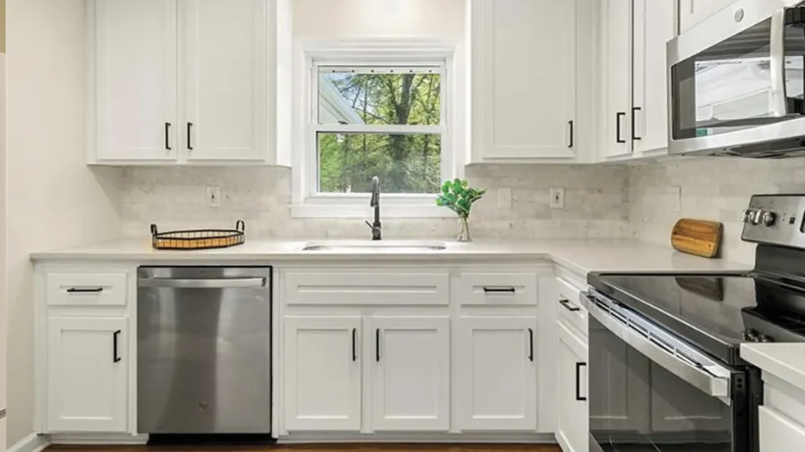 Modern white kitchen with stainless steel appliances, marble backsplash, and window overlooking greenery.