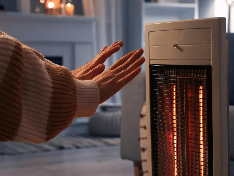 Person warming hands near an electric heater in a cozy room with lit candles and soft lighting.
