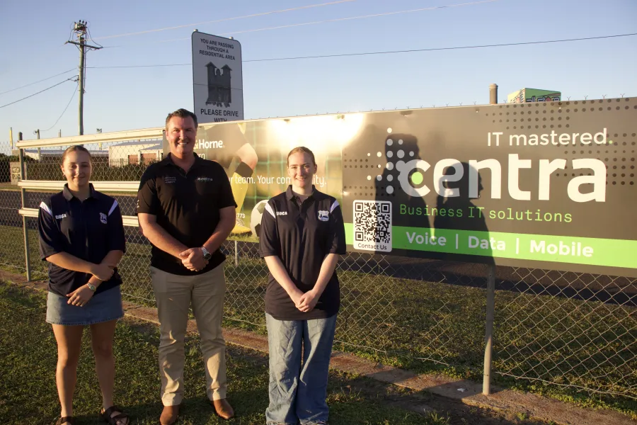 Three people standing in front of a fence with a large Centra IT Business Solutions banner at sunset.