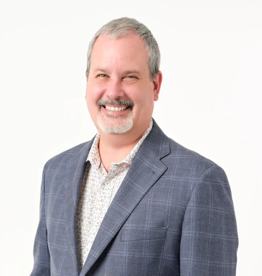 Smiling middle-aged man with gray hair and goatee wearing blue plaid blazer and patterned shirt