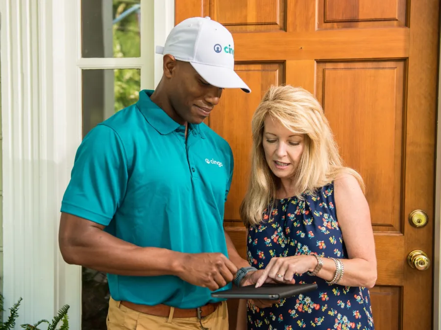 Delivery worker in uniform assisting woman at her front door with a digital tablet.